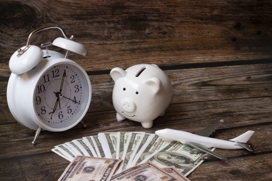 מטוס, שטרות כסף, קופת חיסכון חזיר ושעון על גבי שולחן עץ